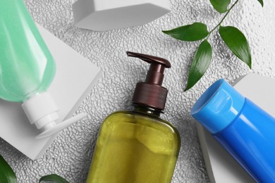 Photo of Different face cleansing products and green leaves on white textured table, flat lay