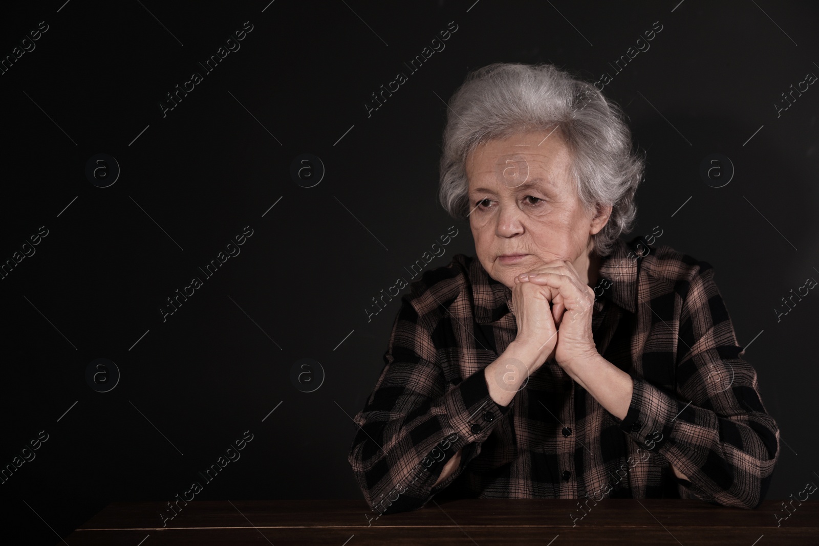 Photo of Poor upset woman sitting at table on dark background. Space for text