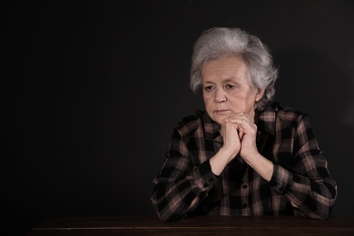 Photo of Poor upset woman sitting at table on dark background. Space for text