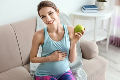 Young pregnant woman holding apple at home