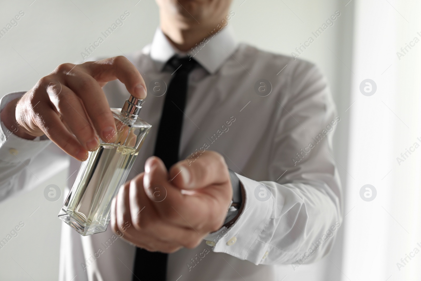 Photo of Man applying perfume on wrist indoors, closeup