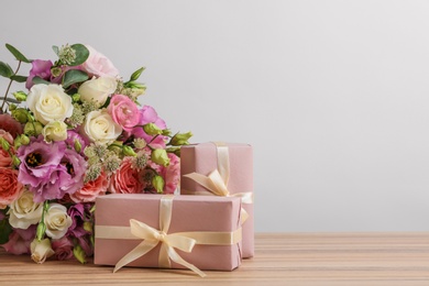 Beautiful bouquet of flowers and gift boxes on wooden table against light background. Space for text