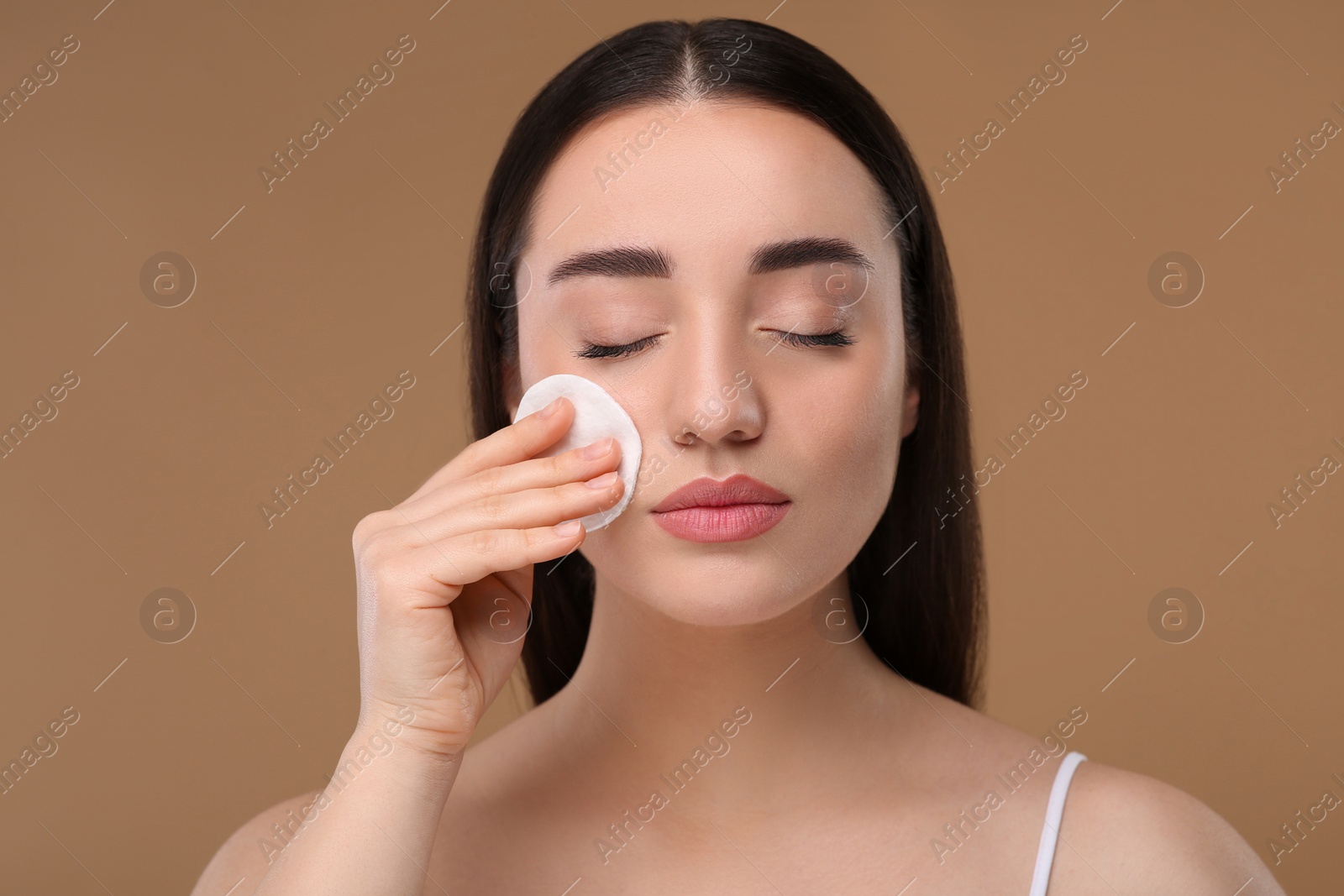 Photo of Beautiful woman removing makeup with cotton pad on beige background