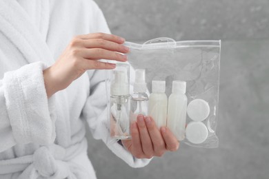 Photo of Woman holding plastic bag of cosmetic travel kit against grey wall, closeup. Bath accessories
