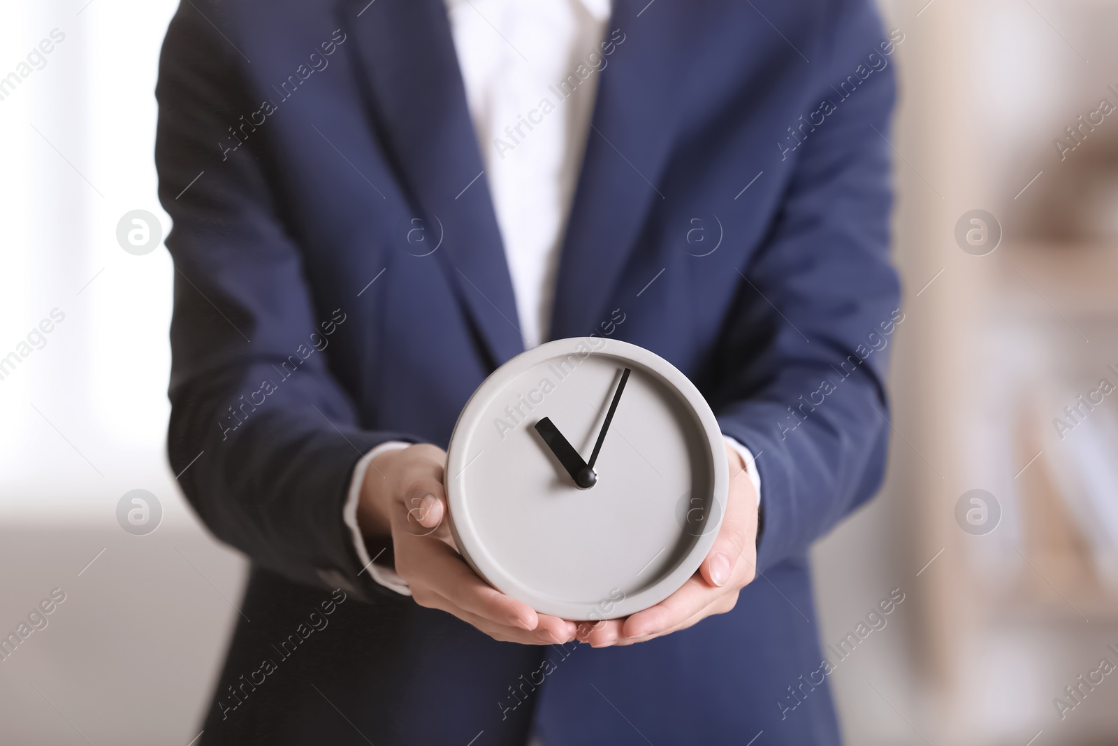 Photo of Businesswoman holding alarm clock on blurred background. Time concept