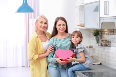 Photo of Beautiful mature lady, daughter and grandchild with gift box in kitchen. Happy Women's Day