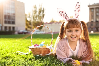 Photo of Cute little girl with bunny ears and basket of Easter eggs in park