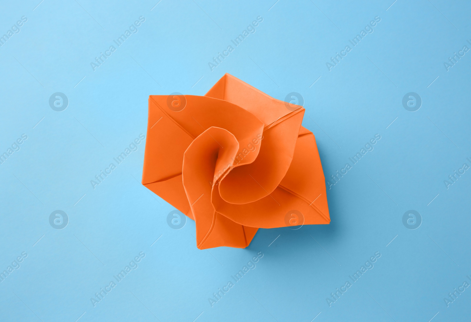 Photo of Origami art. Handmade orange paper flower on light blue background, top view