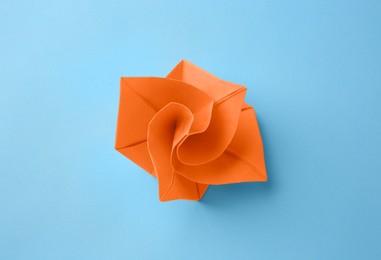 Origami art. Handmade orange paper flower on light blue background, top view
