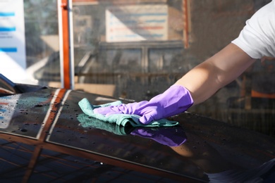 Worker cleaning automobile with rag at car wash, closeup