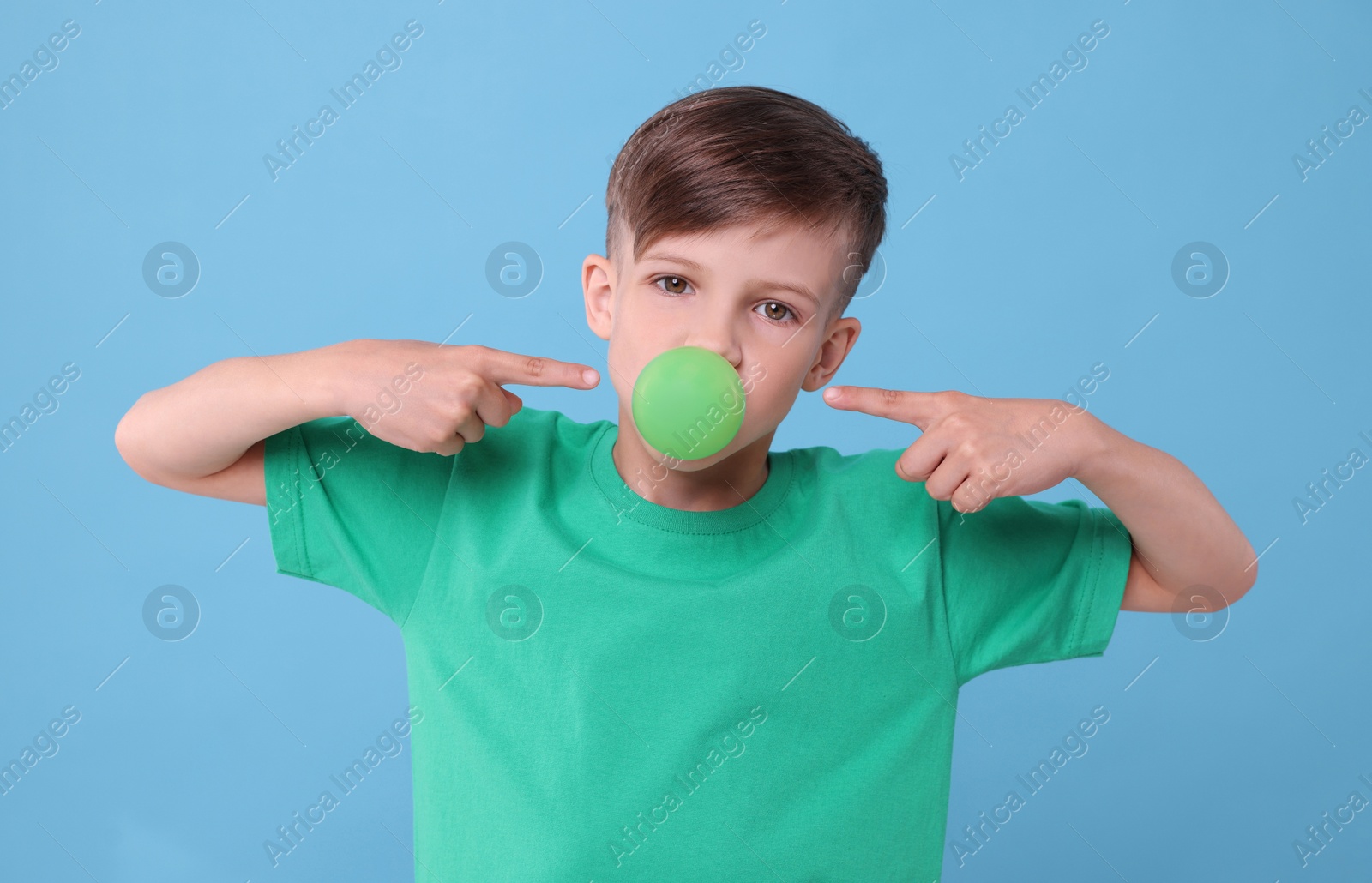 Photo of Boy blowing bubble gum on light blue background