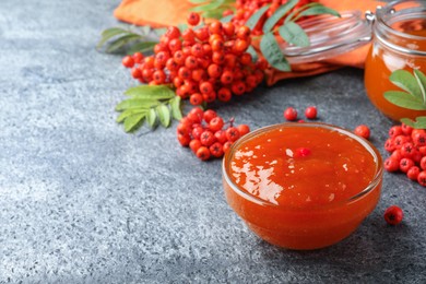 Photo of Delicious rowan jam in glass bowl and berries on grey table. Space for text