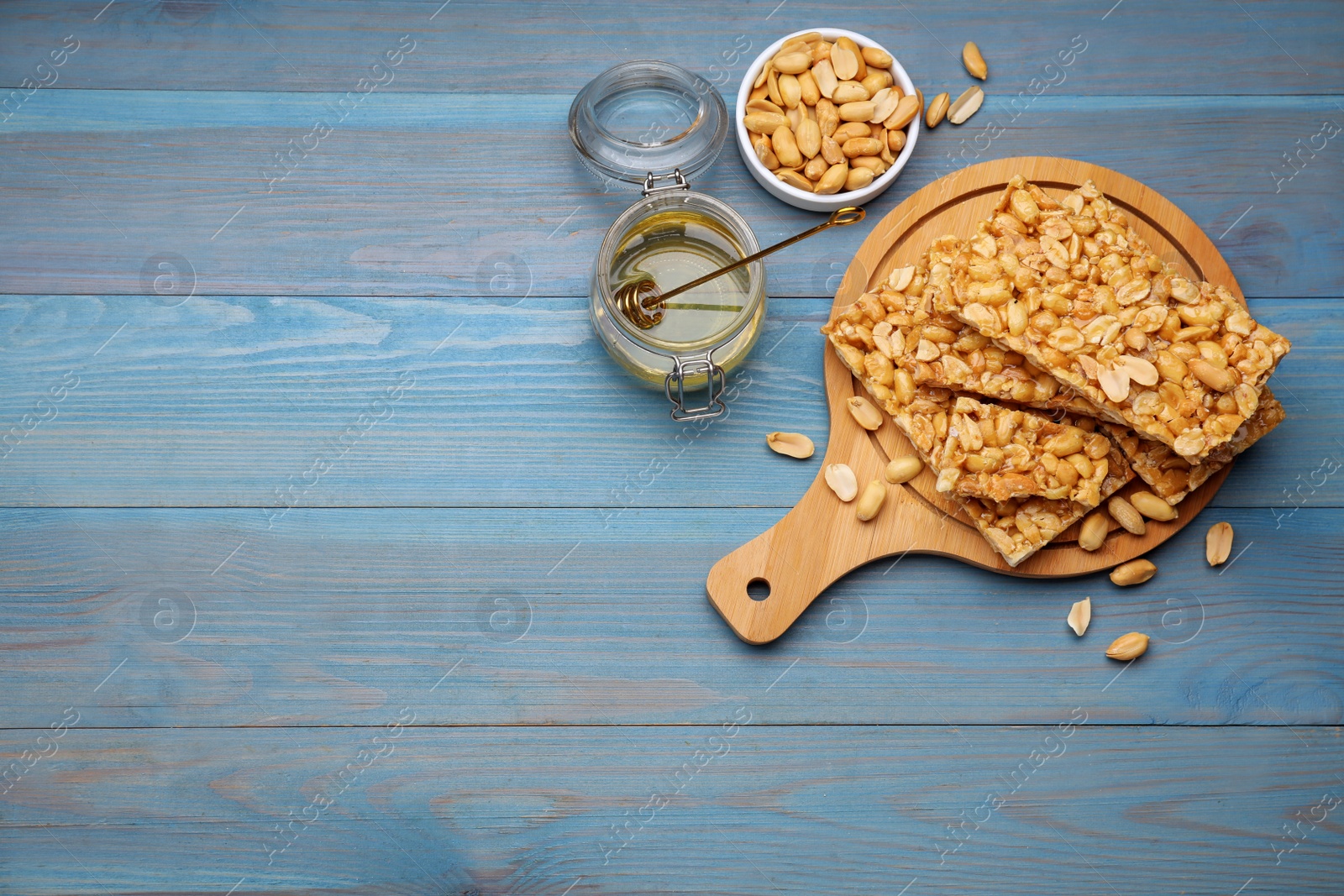 Photo of Delicious peanut bars (kozinaki) and ingredients on light blue wooden table, flat lay. Space for text