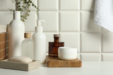 Photo of Different bath accessories and personal care products on white table near tiled wall