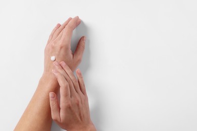 Woman with cosmetic cream on hand against white background, top view. Space for text