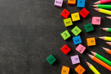 Photo of Many colorful cubes with numbers, multiplications and pencils on dark grey table, flat lay. Space for text