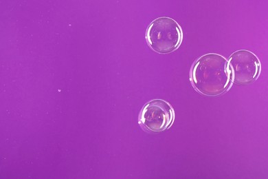 Beautiful transparent soap bubbles on violet background, space for text