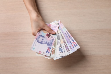 Woman holding Ukrainian money on wooden background, closeup