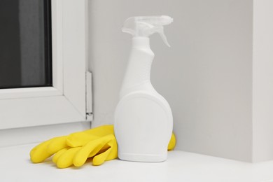 Photo of Spray bottle of cleaning product and rubber gloves on window sill indoors
