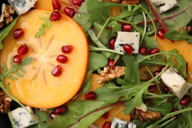 Tasty salad with persimmon, blue cheese, pomegranate and walnuts as background, top view