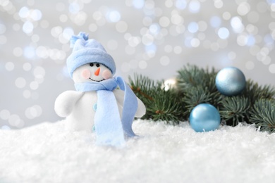 Photo of Snowman toy and Christmas tree branch with balls on snow against blurred festive lights