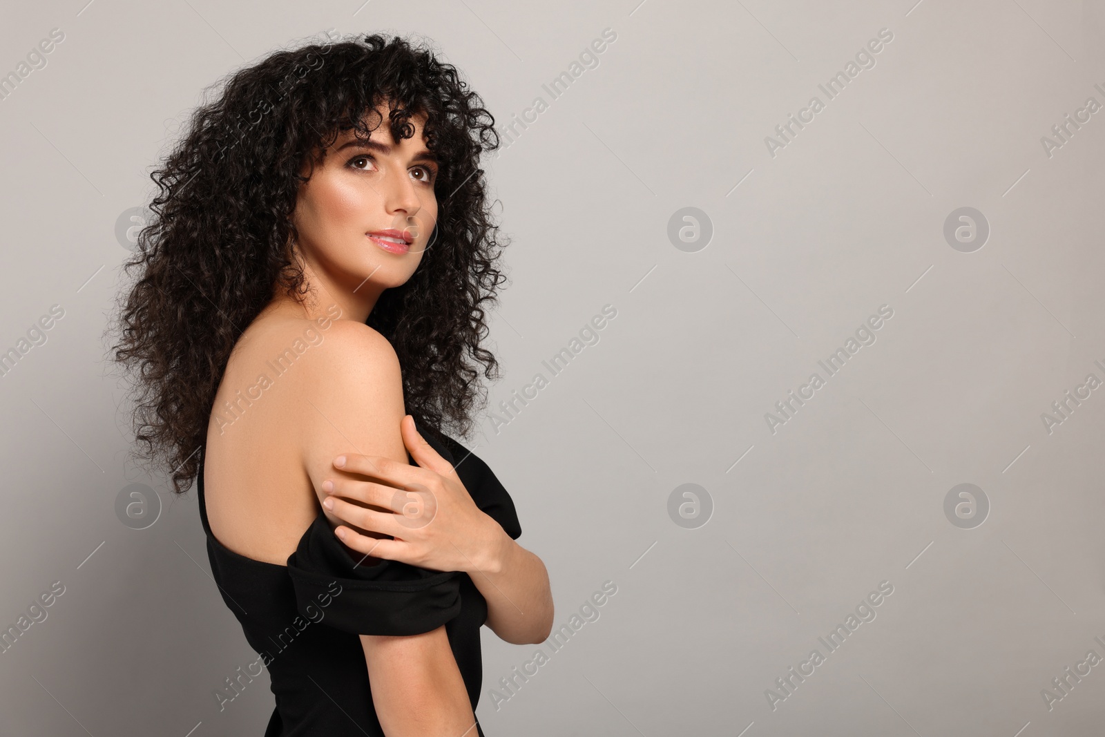 Photo of Beautiful young woman with long curly hair on light grey background. Space for text