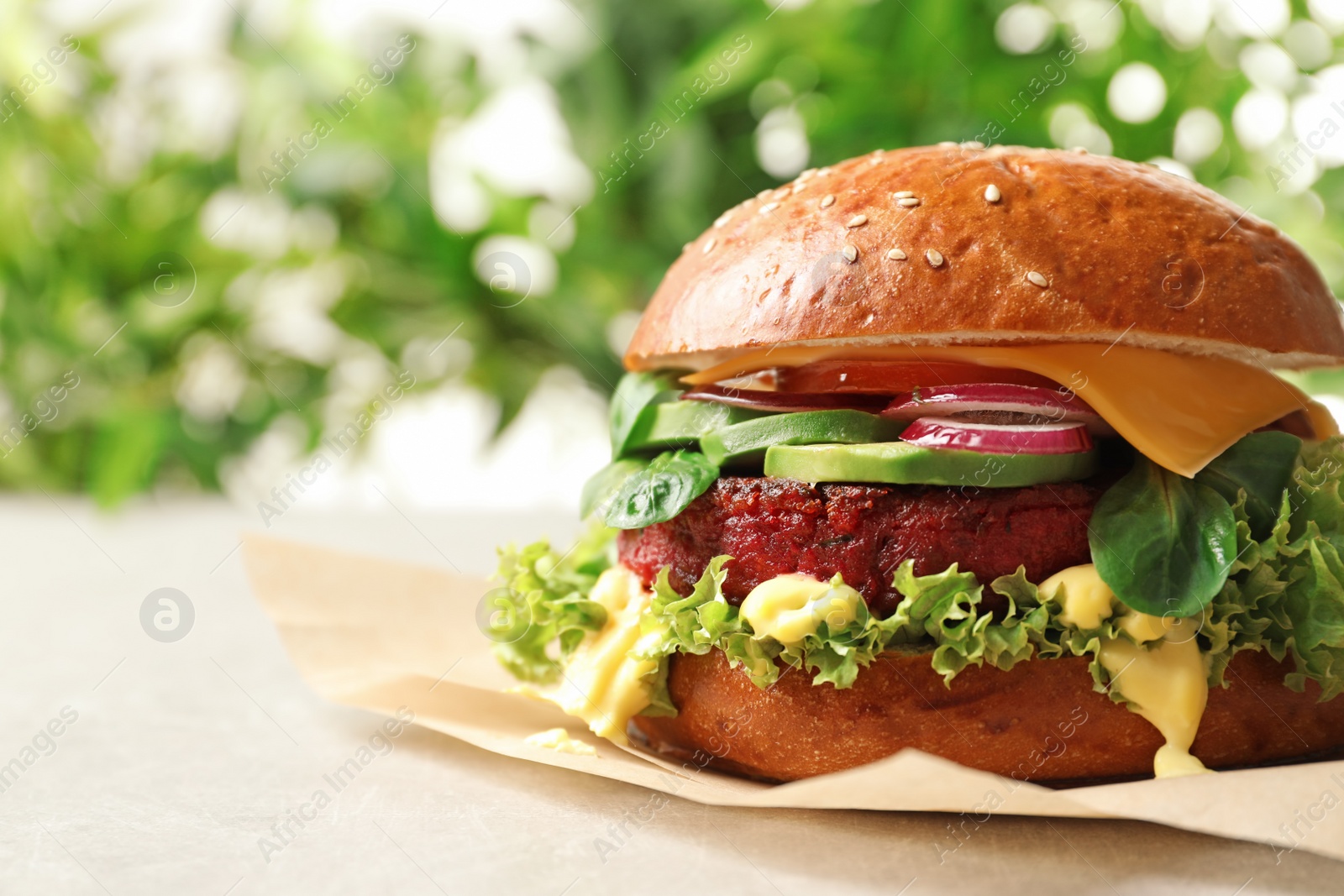 Photo of Tasty vegetarian burger with beet cutlet on table against blurred background. Space for text