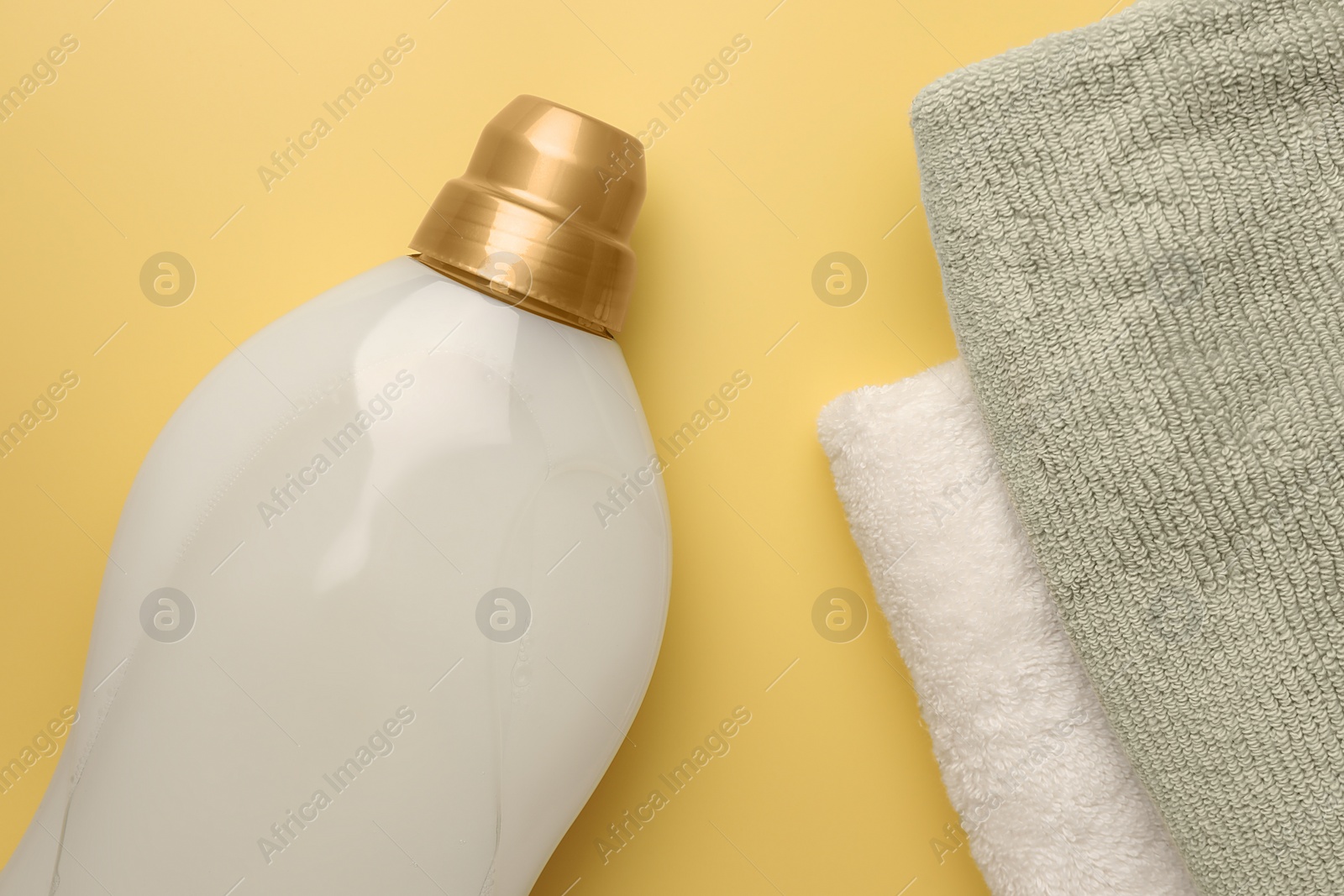 Photo of Bottle of fabric softener and towels on pale yellow background, flat lay