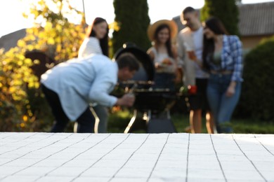 Photo of Empty white wooden table and blurred view of friends having barbecue party outdoors. Space for text