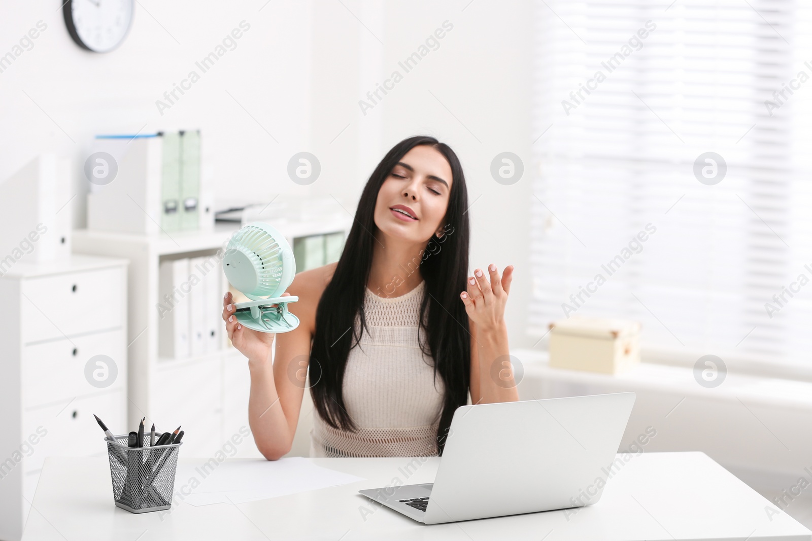 Photo of Young woman enjoying air flow from fan at workplace