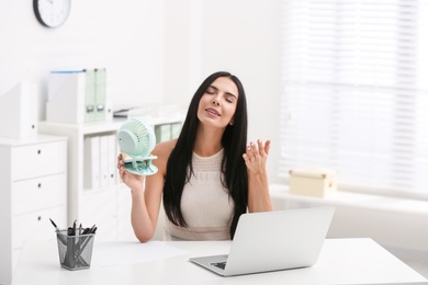 Photo of Young woman enjoying air flow from fan at workplace