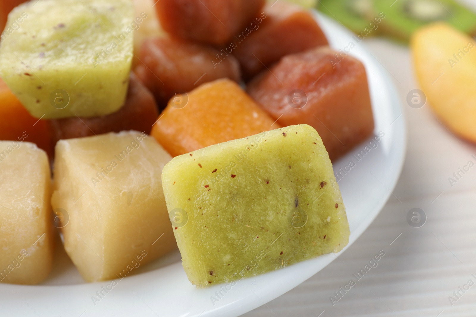 Photo of Different frozen fruit puree cubes on white wooden table, closeup