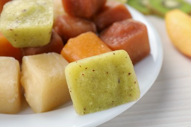 Photo of Different frozen fruit puree cubes on white wooden table, closeup