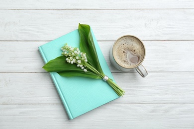 Flat lay composition with notebook, lily of the valley bouquet and coffee on white wooden background