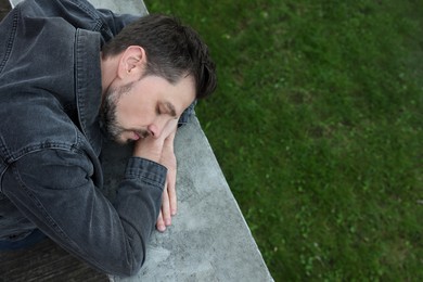 Photo of Tired man sleeping on stone parapet outdoors, top view. Space for text