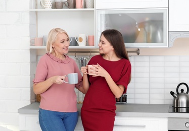 Photo of Portrait of mature woman and her daughter drinking tea in kitchen
