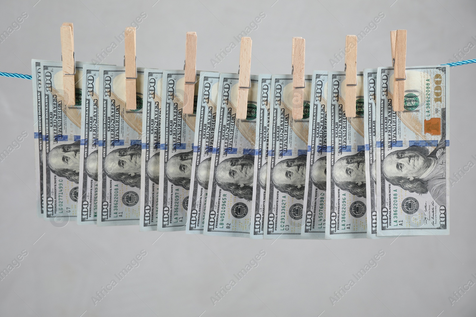 Photo of Dollar banknotes hanging on rope against light grey background