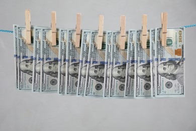 Dollar banknotes hanging on rope against light grey background