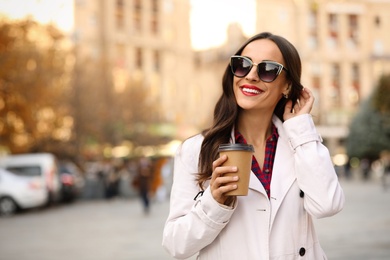 Photo of Beautiful woman with cup of coffee on city street. Autumn walk