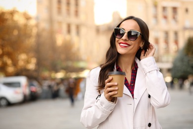 Beautiful woman with cup of coffee on city street. Autumn walk