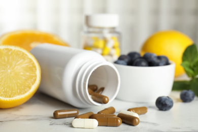 Photo of Bottle with vitamin pills, blueberries and lemon on white marble table