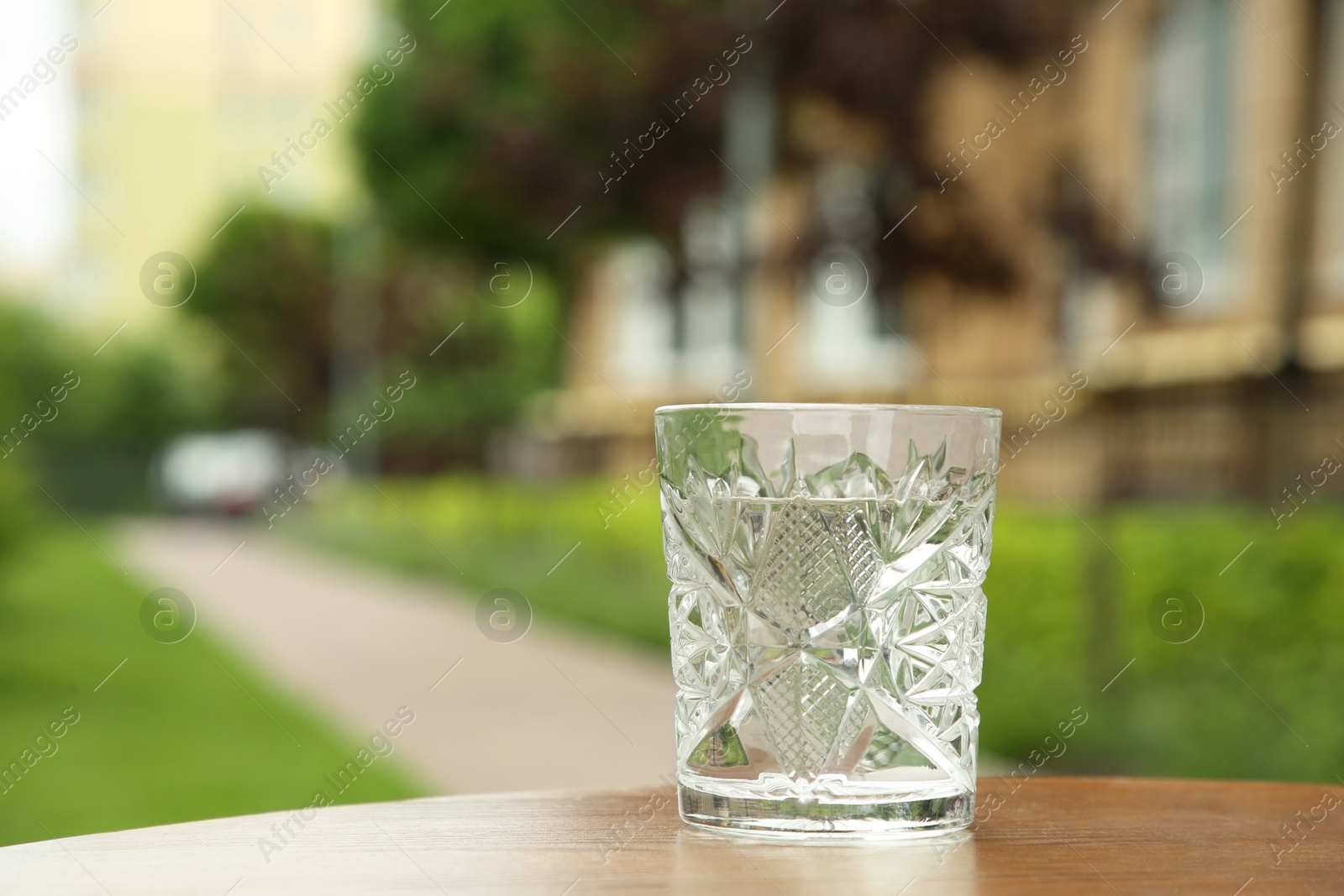 Photo of Glass of fresh water on wooden table outdoors, space for text