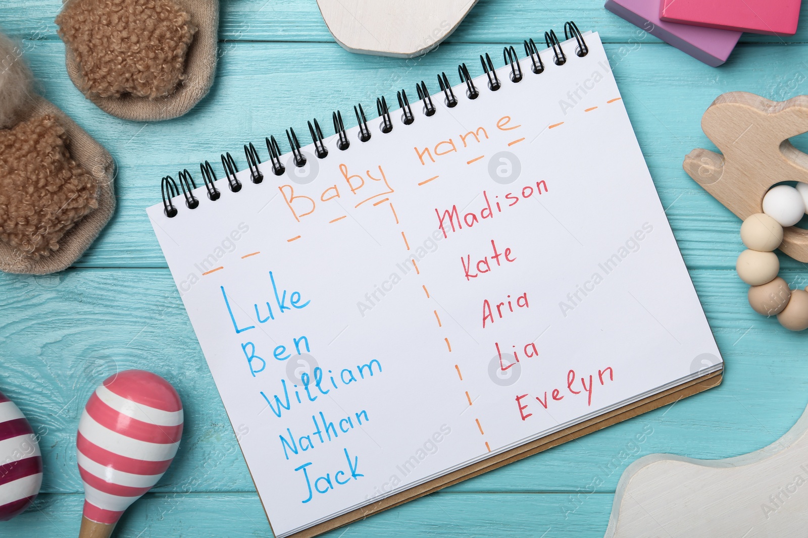 Photo of Notebook with different baby names and toys on light blue wooden table, flat lay