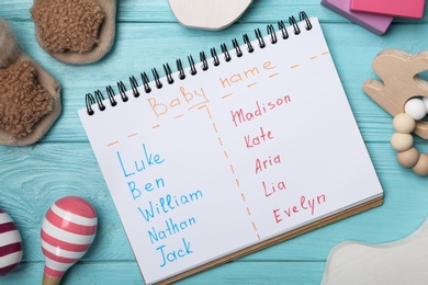 Notebook with different baby names and toys on light blue wooden table, flat lay