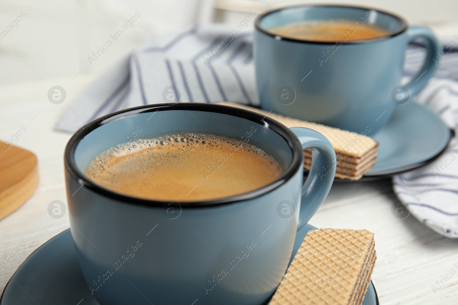 Photo of Delicious wafers and coffee for breakfast on white wooden table, closeup