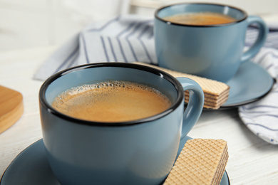 Photo of Delicious wafers and coffee for breakfast on white wooden table, closeup