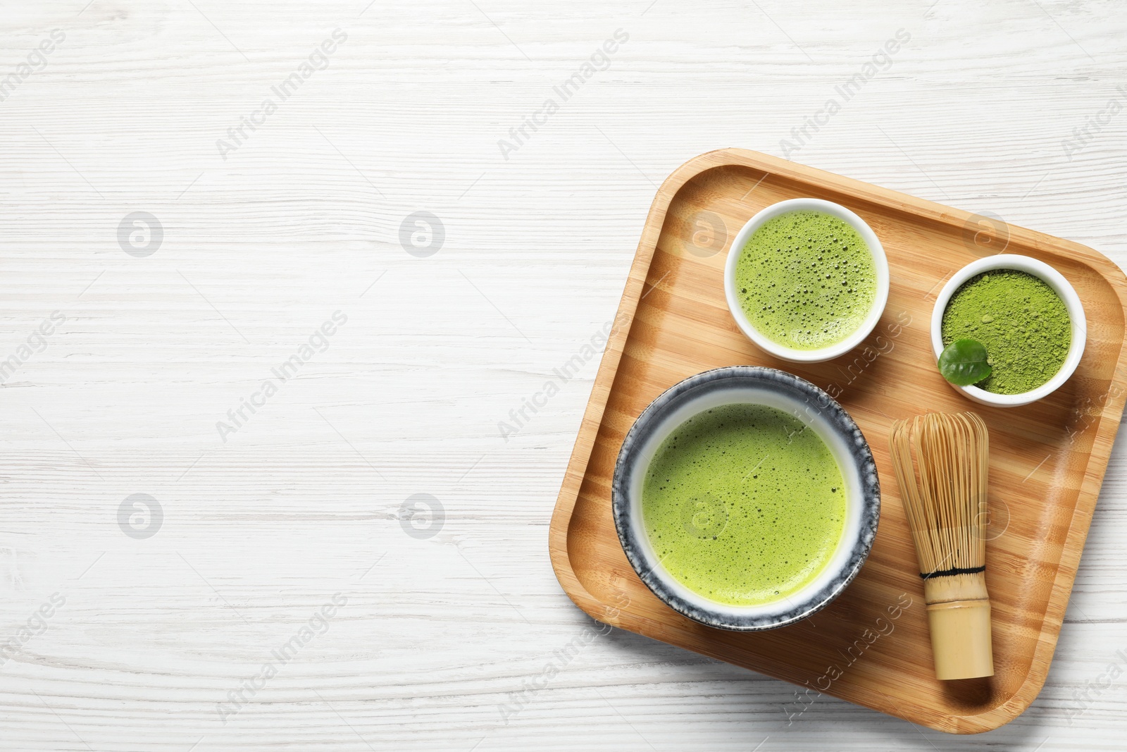 Photo of Fresh matcha tea, bamboo whisk and green powder on white wooden table, top view. Space for text