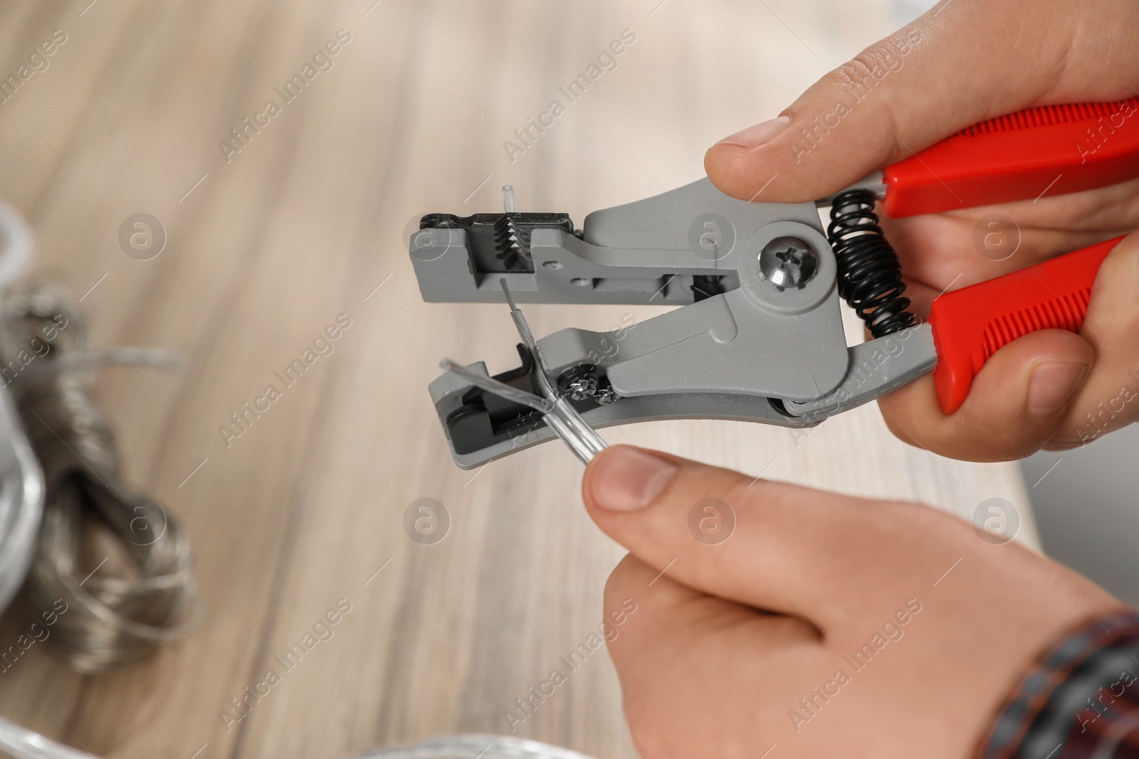 Photo of Professional electrician stripping wiring at wooden table, closeup