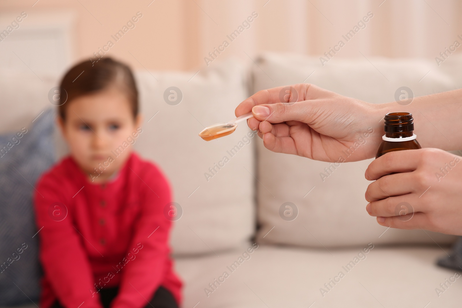 Photo of Mother with cough syrup for her daughter in room, focus on hands