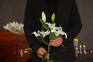 Photo of Young man with white lilies in funeral home, closeup